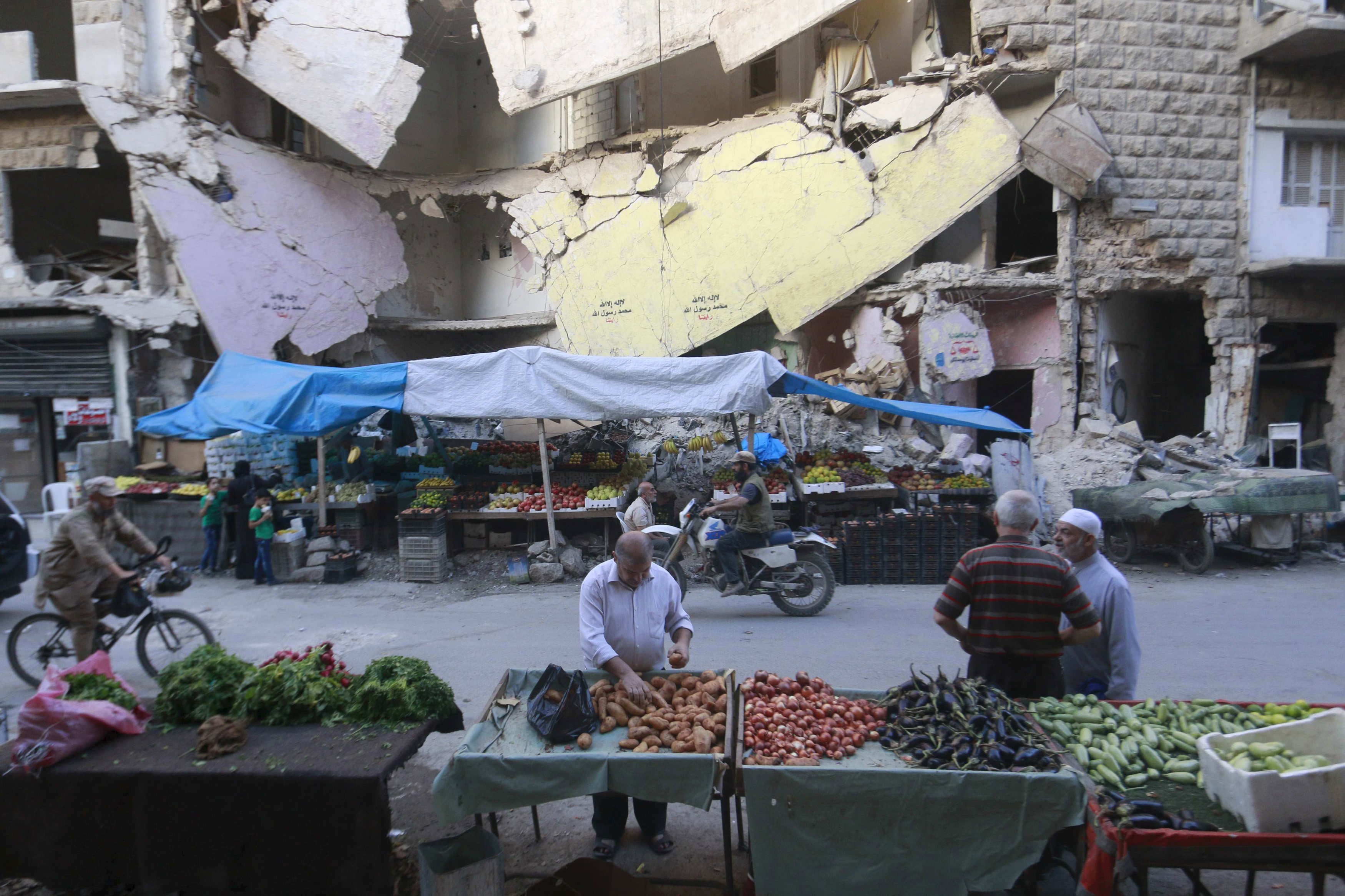 Warga berbelanja sayuran dan buah-buahan yang dijual di depan gedung rusak di wilayah Bustan al-Qasr, Aleppo, Suriah, Rabu (14/10). ANTARA FOTO/REUTERS/Hosam Katan.