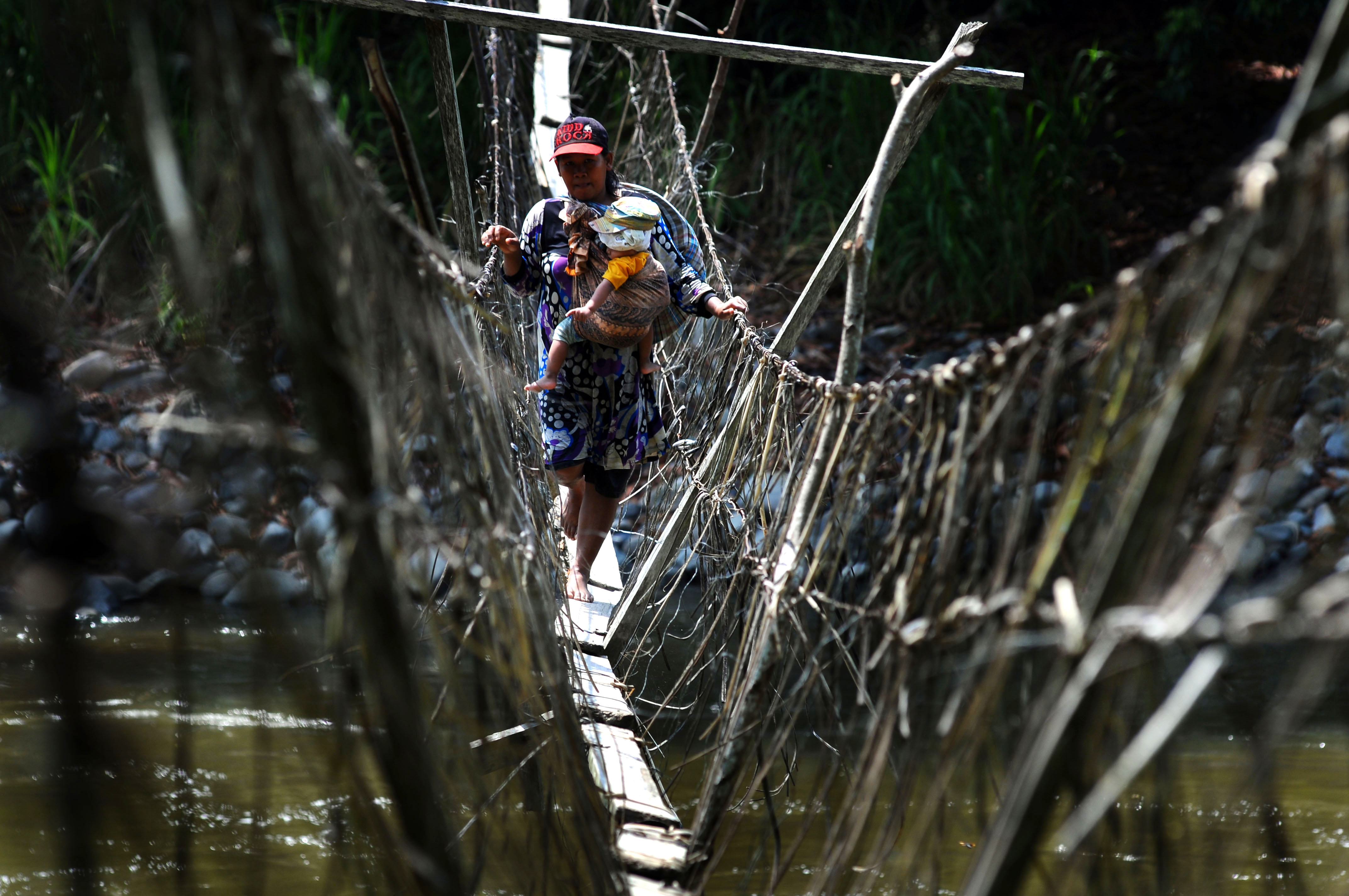 Seorang ibu sambil menggendong anaknya meniti jembatan darurat  di Desa Makujawa, Gimpu, Sigi, Sulawesi Tengah, Sabtu (7/11). Jembatan darurat yang panjangnya kurang lebih 300 meter itu satu-satunya akses untuk menuju dusun satu Wahi dan perkebunan masyarakat. ANTARA FOTO/Fiqman Sunandar.